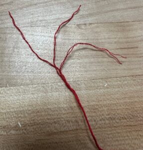 Red embroidery thread unraveled from one strand into three strands.