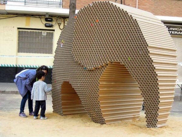 Two people stand next to a life size elephant made entirely from cardboard.