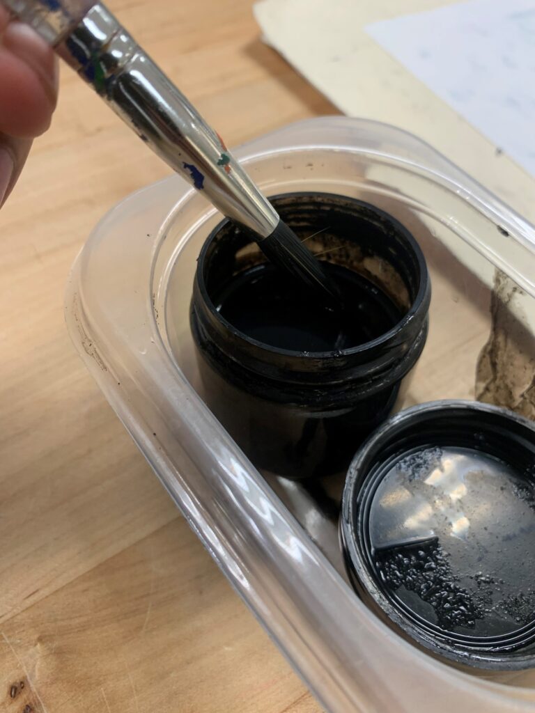 A round brush dipped into a small container of black ink.