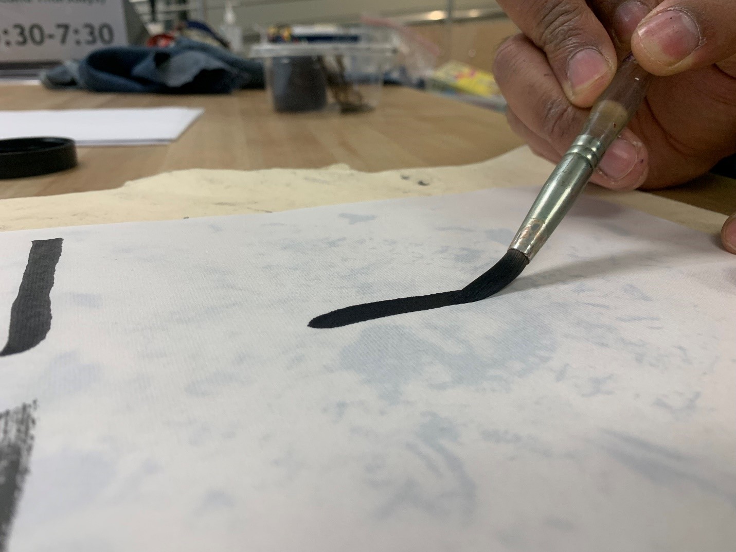 A calligraphy brush making a black mark of ink on a piece of paper.