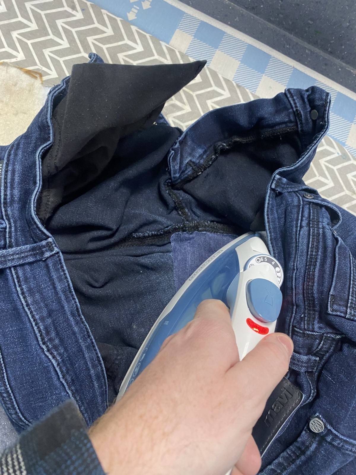 Hand holding an iron over a dark denim patch over dark denim jeans