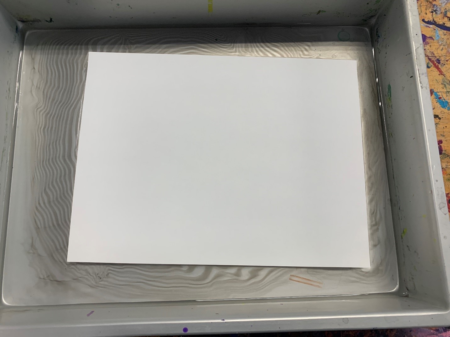 One piece of white paper floating on the water/ink design in tray