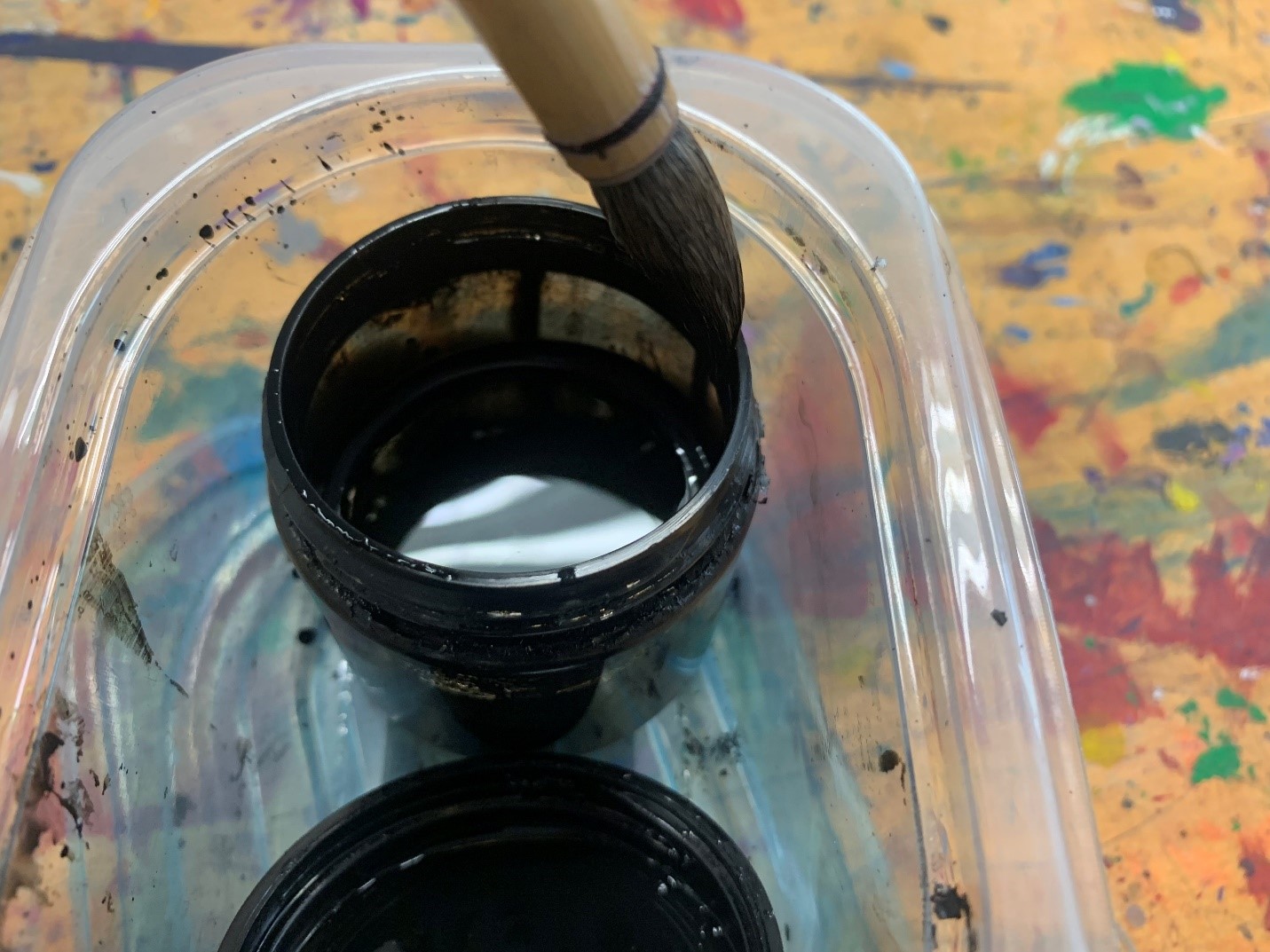 Calligraphy brush exiting the pot of ink by being brushed on the rim