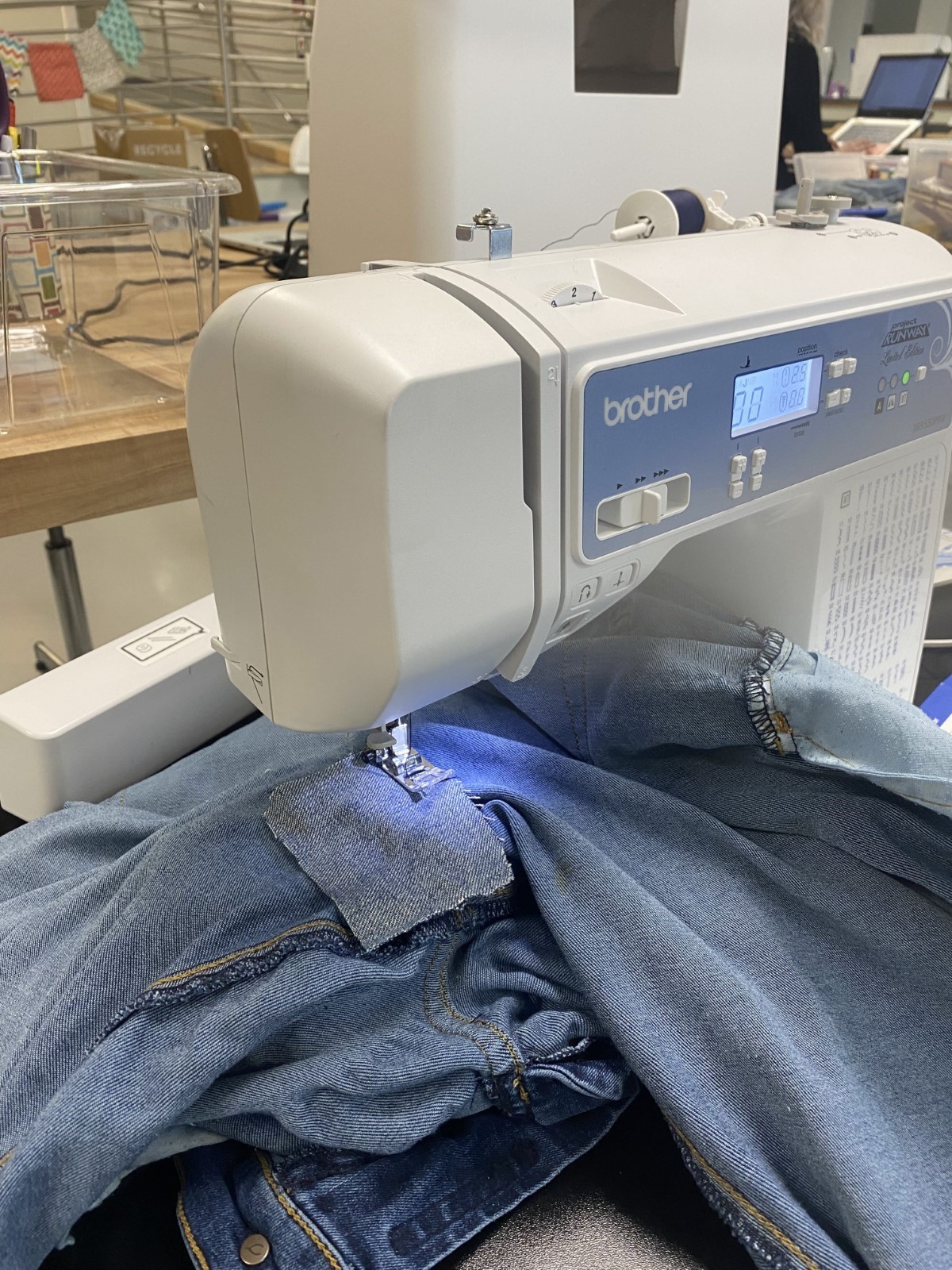 pair of jeans positioned under needle of sewing machine with a denim patch on top