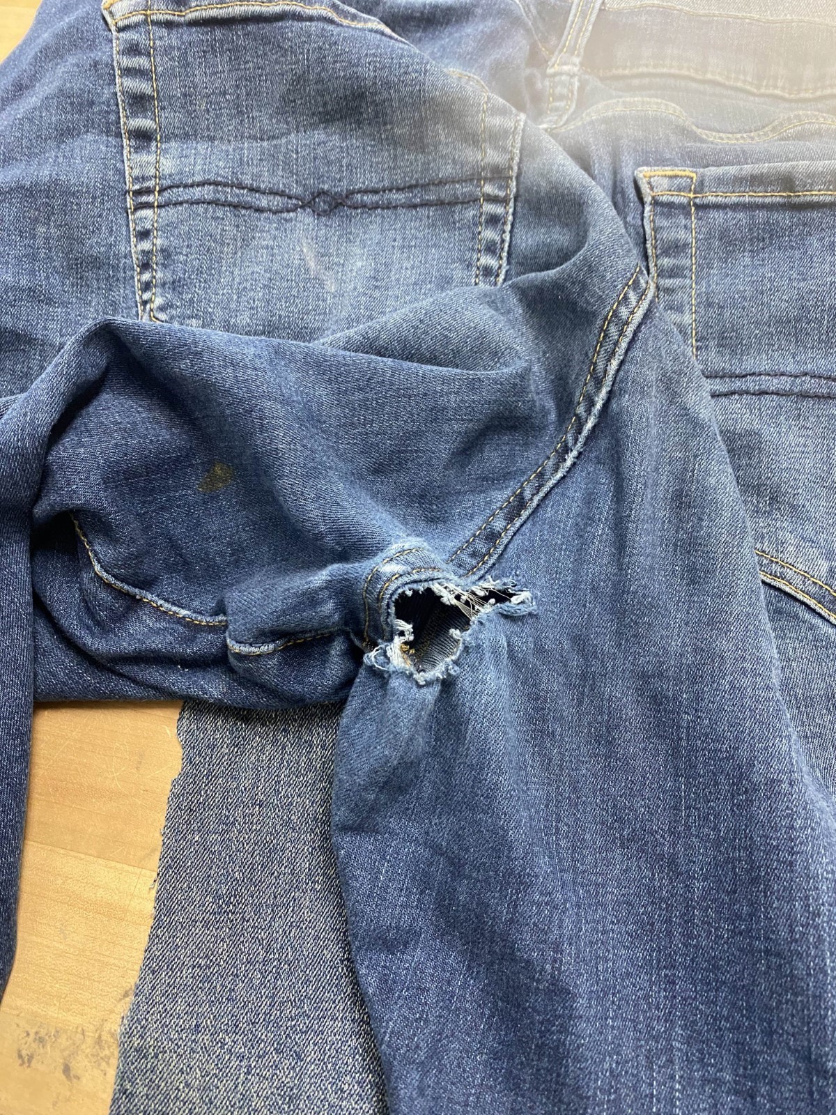 A pair of blue jeans with a hole near the rear center seam.