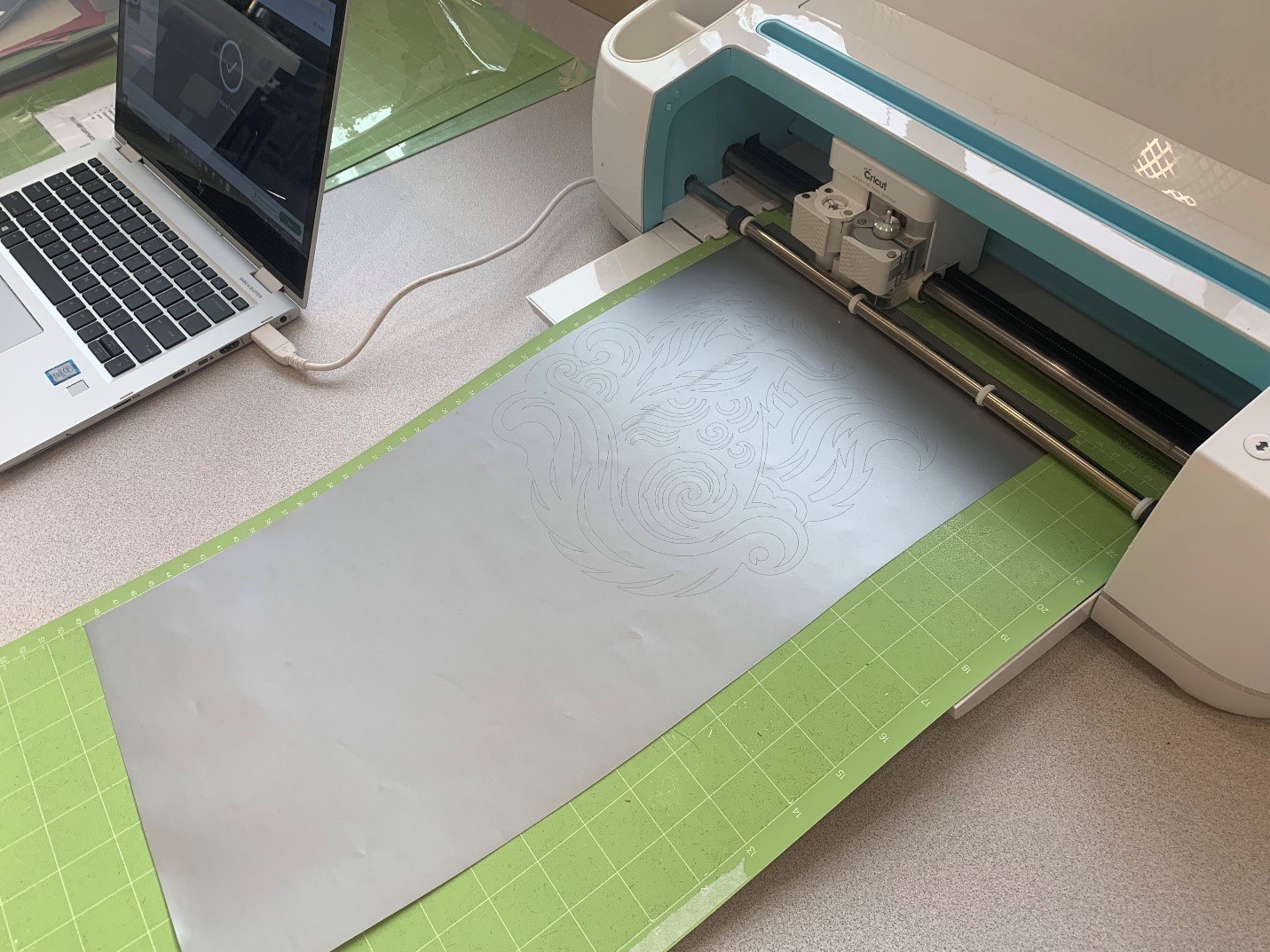 Silver vinyl loaded on a mat and fed into the Cricut Maker as it cuts the wolf design.