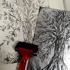 An ink roller and two sheets of paper depicting a lithograph of a tree.