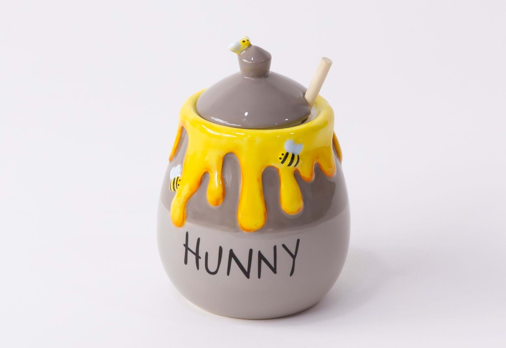 A small grey clay jar with a lid and yellow drips that reads "Hunny"