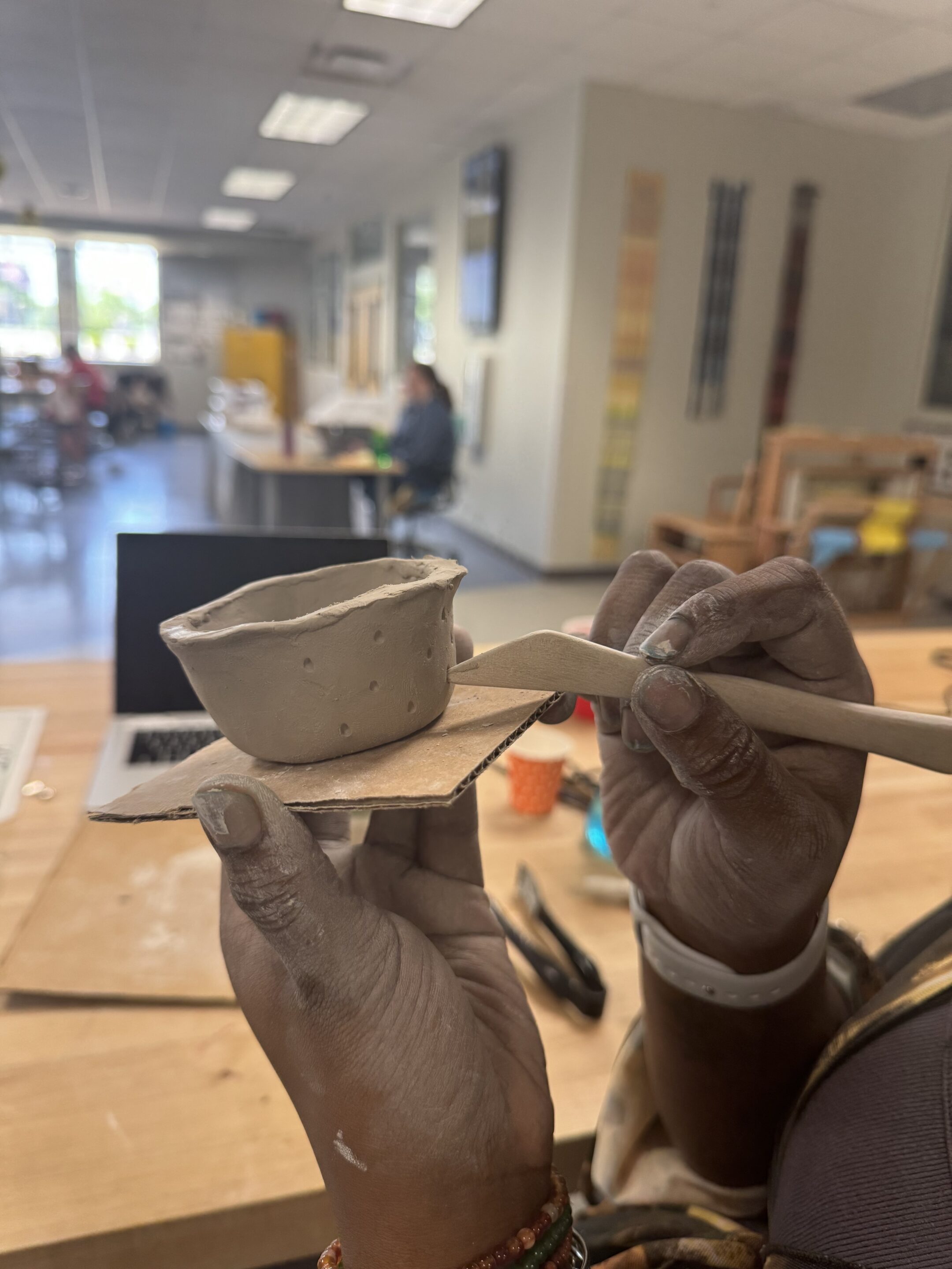 A side view of a small clay bowl with a hand using a wooden tool to create a design on its outside