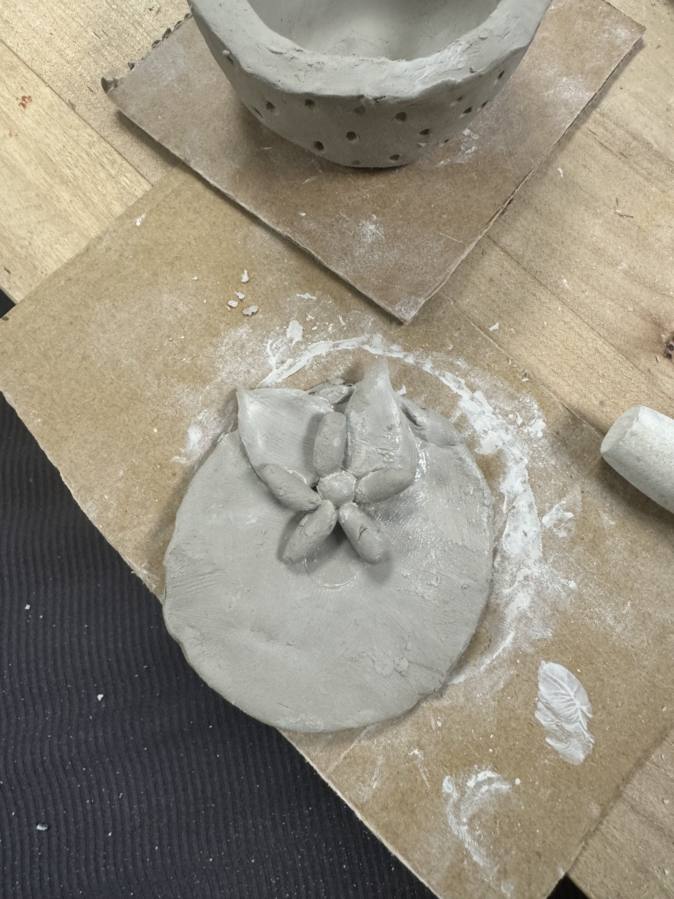 A flat round piece of clay with a little grey clay leaves on one side