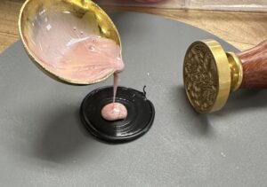 Pink wax being poured onto a flat blank seal. 