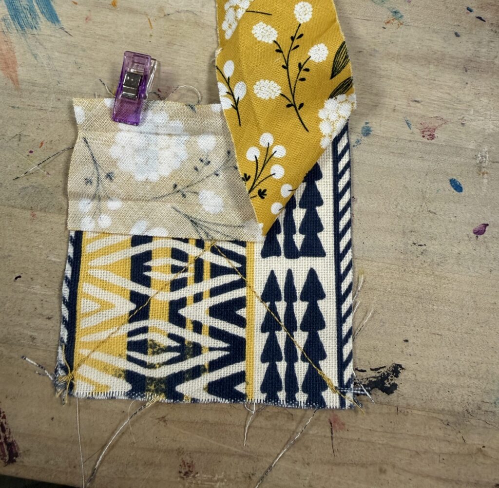 Bias tape clipped to fabric square coaster with the bias strip folded up at the end to make a mitered corner. 