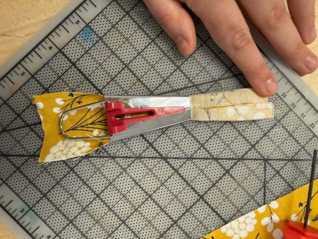Fabric being fed through a bias tape maker. 