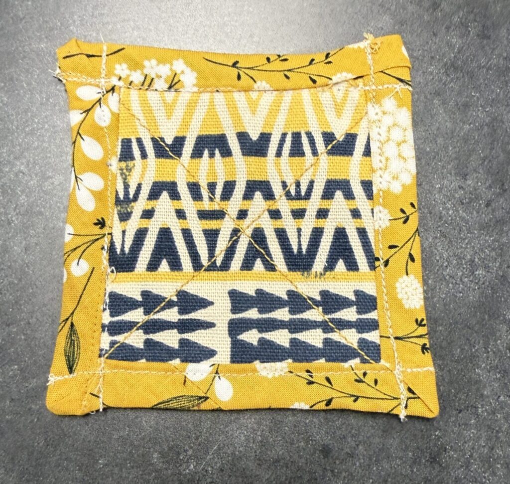 A finished square fabric coaster with bias tape along the outside. 