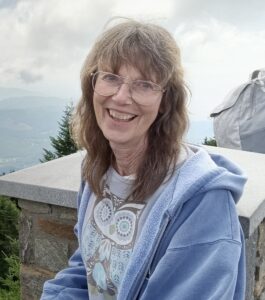 A photo of a woman in a blue jacket and glasses smiling