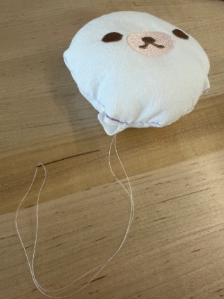 Stuffed plush head with hand sewing needle and thread attached. 