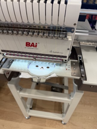 Face embroidered onto white fabric inside embroidery frame in machine.