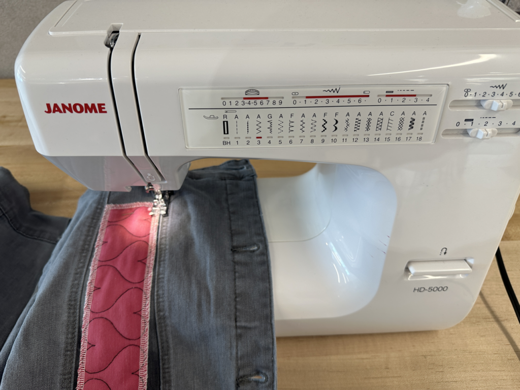 Janome sewing machine with section of jean jacket and fabric being sewn together.